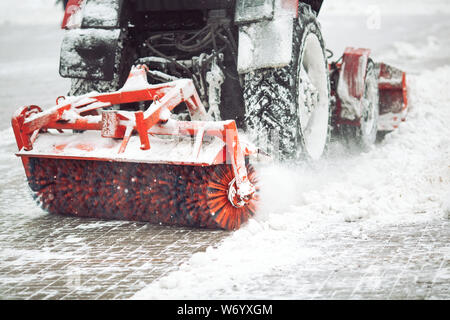City service cleaning snow , a small tractor with a rotating brush clears a road in the city park from the fresh fallen snow on winter day Stock Photo