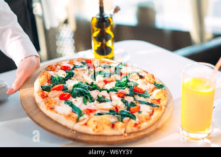 The waiter puts pizza On the table in the Restaurant. Stock Photo