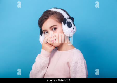 happy little cute girl wearing earmuffs on blue background Stock Photo