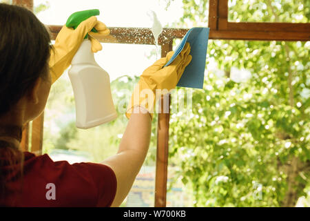 Girl in yellow gloves with a detergent washes plastic windows. Cleaning company for home and window cleaning. Stock Photo