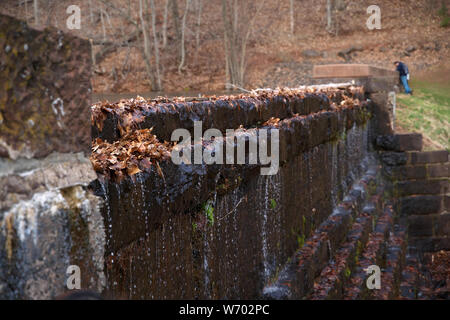 Water slowly seeping out from a reservoir wall as a couple watches on at a safe distance. Stock Photo