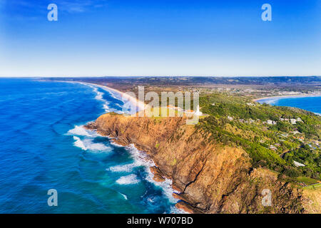 WHIte stone lighhouse at the top of steep sandstone cliff on Pacific coast of Australia in Byron Bay town view from above inland - the most eastern po