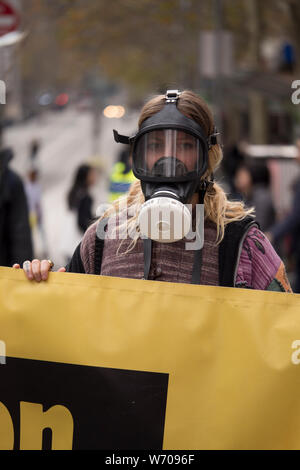 Woman wearing a black gas mask holding a bright yellow Climate Emergency banner disruption traffic in downtown Melbourne, Australia. Stock Photo