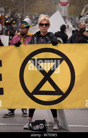 Young blonde woman in black sunglasses and black leather jacket defiantly holding holding a large yellow Climate Emergency banner. Stock Photo
