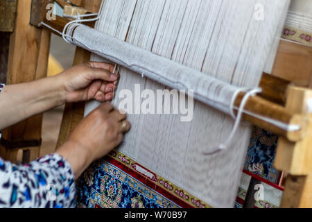 Carpet weaving close up. Senior woman's hand weaves traditional manual silk carpet loom Stock Photo