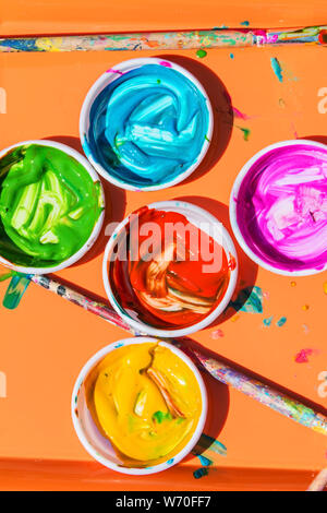Ceramic bowls filled with colorful paints and paint brushes sit on paper for kids to use to paint with at a festival. Stock Photo