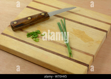Chopped chives and fresh rinsed chive sprigs and kitchen knife on wooden cutting board Stock Photo