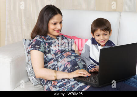 Pregnant mother assisting her son in using a laptop Stock Photo