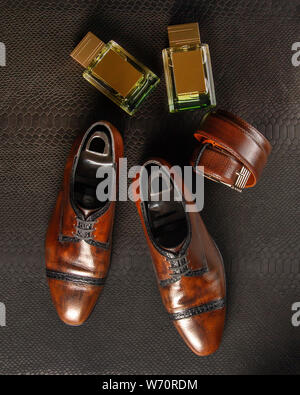 Composition of a pair of men's shoes of brown color, two bottles of men's perfume and men's trouser belt against the background of black python leathe Stock Photo