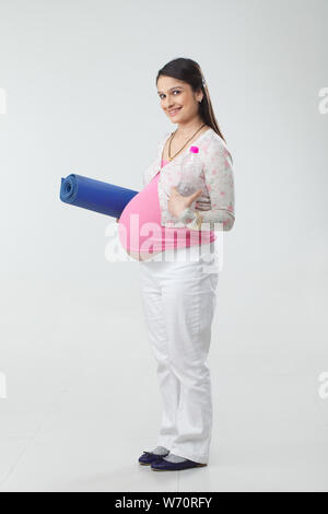 Pregnant woman holding yoga mat and water bottle Stock Photo