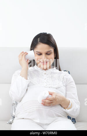 Pregnant woman holding tin can phone to ear Stock Photo