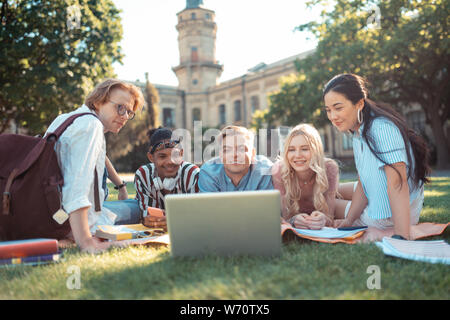 Groupmates lying on a grass lawn watching a movie. Stock Photo