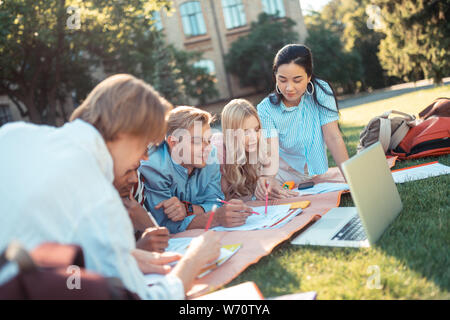 Students working on their hometasks lying on the grass. Stock Photo