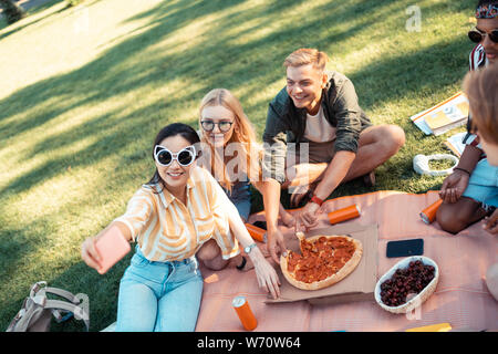 Cheerful friends taking selfies and eating pizza. Stock Photo