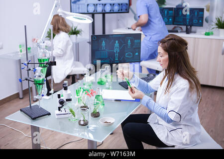 Female scientist holding a green solution while hear team works in the background. Young biologist in the background. Stock Photo