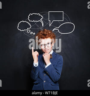 Smart schoolboy pointing at empty speech clouds bubbles on chalkboard background Stock Photo
