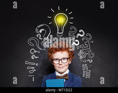 Smart child boy in glasses smiling and holding book on background with lightbulb Stock Photo