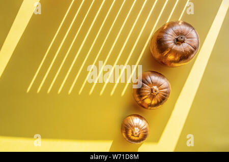 Three golden decorative pumpkins on a yellow background. Halloween concept. Hard shadows, bright sunlight. Stock Photo