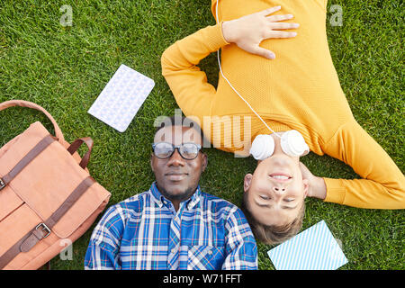 Above view portrait of two students lying on green grass and looking at camera, copy space Stock Photo