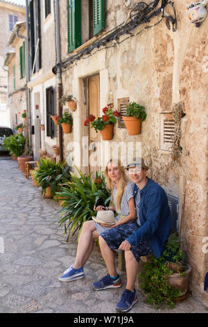 young couple sitting on bench on romantic mediterranean street Stock Photo