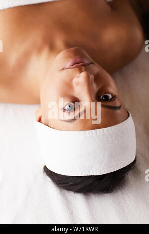 High angle portrait of beautiful mixed-race woman lying on massage table and looking at camera while enjoying SPA, copy space Stock Photo