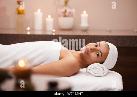 Portrait of beautiful mixed race woman smiling blissfully while lying on massage table in spa, copy space Stock Photo