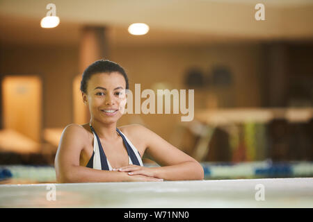 Portrait of beautiful mixed race woman relaxing in swimming pool and smiling at camera, copy space Stock Photo