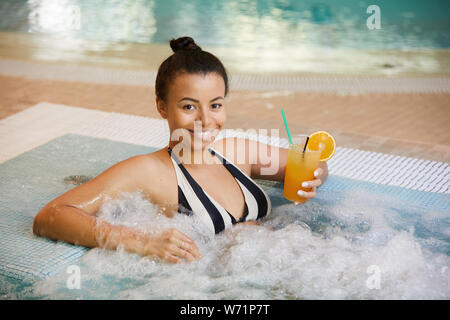 Portrait of beautiful woman drinking cocktail in bubbly hot tub and smiling at camera, copy space Stock Photo