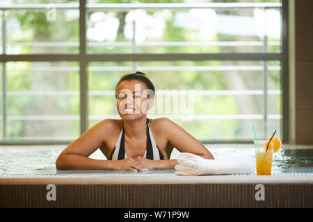 Portrait of happy mixed race woman enjoying spa in swimming pool, copy space Stock Photo