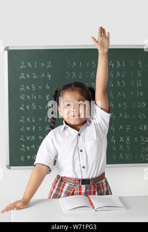 Schoolgirl raising hand in classroom Stock Photo