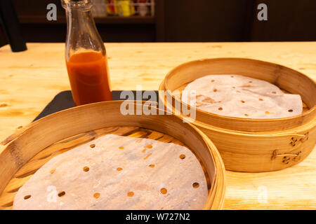 Empty plates and wooden steamer from steamed dumplings on a wooden table with chopsticks in an asian restaurant or chinese bar with dumplings. Stock Photo