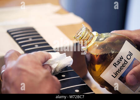 An acoustic guitar being serviced. The technician is treating the wooden fret board with linseed oil. Stock Photo