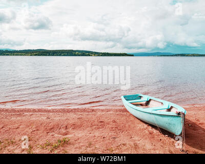 Blue fishing boat anchored on beach sand of lake. Smooth evening water level and calm. Large vallely of Lipno lake. Stock Photo