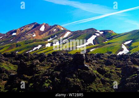 View over field with black volcanic lava ash on mountain range with spots of snow and ice contrasting with blue cloudless sky - Landmannalaugar, Icela Stock Photo