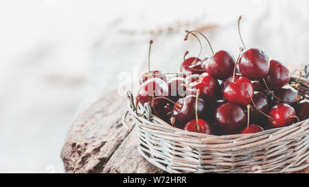 Dark red ripe large cherries in a wicker basket on a wooden table, selective focus. Close up. Copy space Stock Photo
