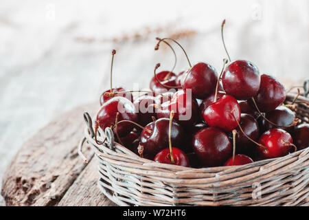 Dark red ripe large cherries in a wicker basket on a wooden table, selective focus. Close up. Copy space. Stock Photo