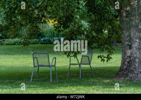 Tranquil scene with two chairs on a green lawn in a park under a hugh tree on a sunny day Stock Photo