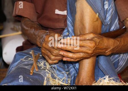Old man with brown skinny hands working with bamboo wood in a paper umbrella factory in Chiang Mai Stock Photo
