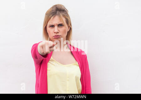 Portrait of serious beautiful blond young woman in yellow shirt and red blouse standing, looking and pointing at camera with serious angry face. indoo Stock Photo