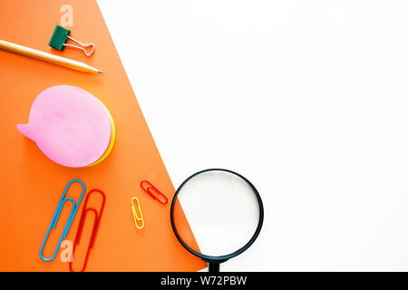 simple pencil, paper clips, magnifier, office stationery in the form of a layout on top of a double background of white and orange. Stock Photo