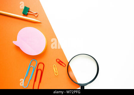 simple pencil, paper clips, magnifier, office stationery in the form of a layout on top of a double background of white and orange. Stock Photo