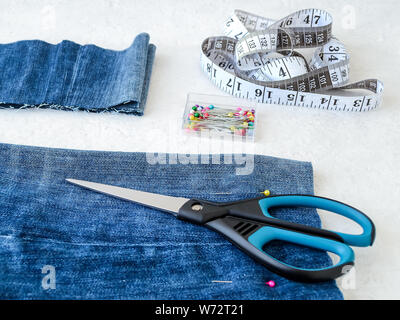Making shorts out of blue jeans with multi colored headed sewing pins, white tailor tape with centimeters and inches and scissors. Shorten the jeans. Stock Photo