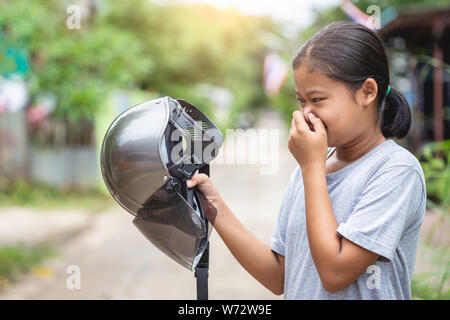 Young asian girl holding brown helmet of motorcycle and smelling. Old helmet concept Stock Photo
