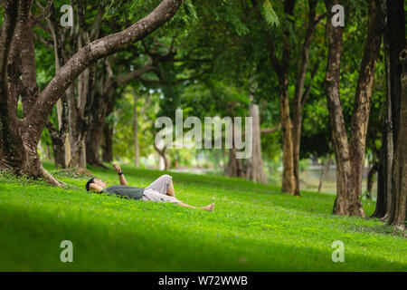 Lifestyle concept : A man laying on the field in the park and looking, checking his smartphone Stock Photo