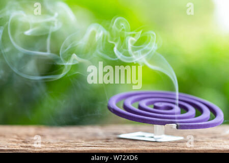 Violet mosquito repellent and white smoke on wooden table with green blur light space background for text, design, photo montage or advertising Stock Photo