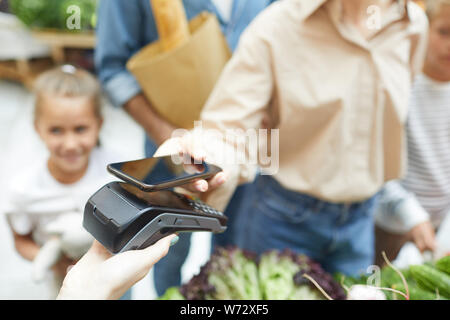 Closeup of young woman paying via smartphone at supermarket while shopping with family, copy space Stock Photo