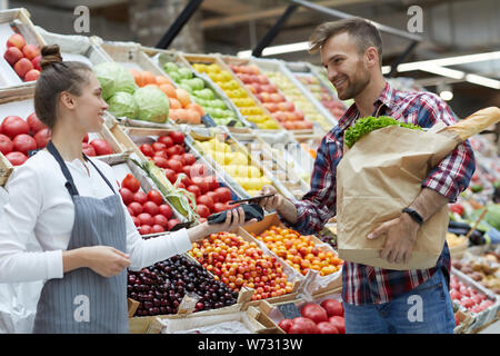 Side view portrait of handsome young man paying via smartphone at farmers market, copy space Stock Photo
