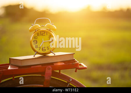 Yellow alarm clock and book put on the Red Japan style classic bicycle at view of green rice field in sunset time Stock Photo