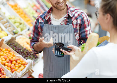 Mid section portrait of young woman paying via smartphone while grocery shopping in supermarket, copy space Stock Photo