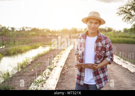 Portrait of young Asian smart farmer holding tablet in his organic farm. Technology and agriculture concept Stock Photo